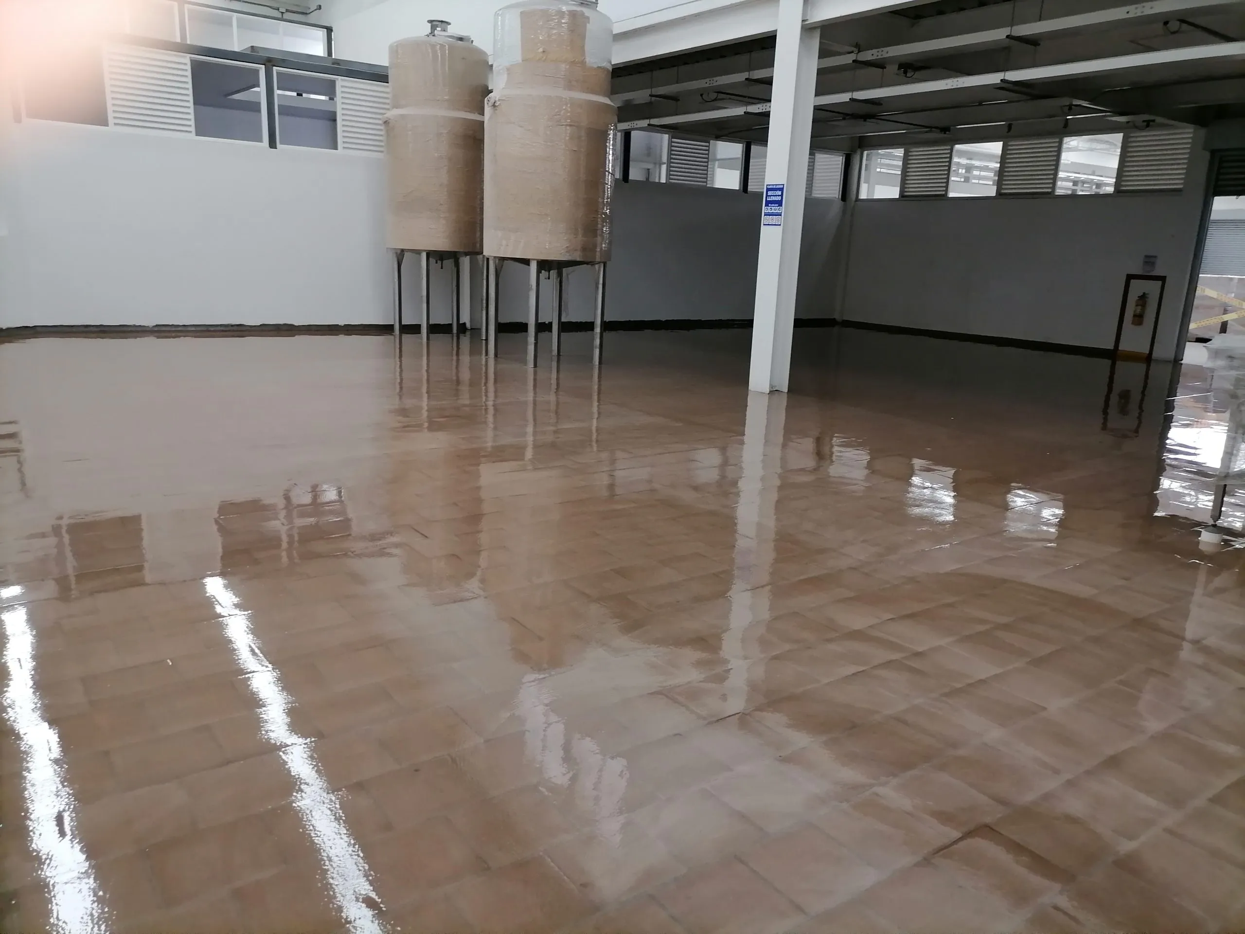 Piso epóxico recién aplicado en una planta industrial, con tanques de proceso al fondo